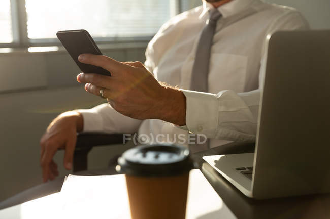 Середня частина красивого молодого керівника чоловічої статі сидить за столом і використовує мобільний телефон в сучасному офісі — стокове фото