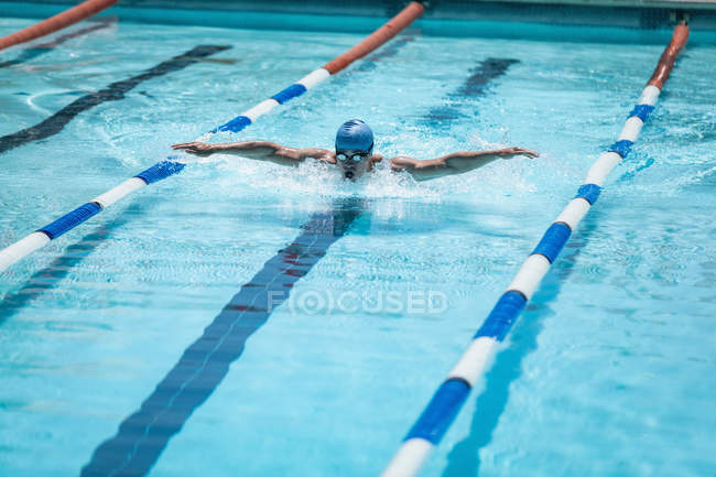 Vista frontal do jovem nadador masculino caucasiano praticando golpe de borboleta na piscina exterior no dia ensolarado — Fotografia de Stock