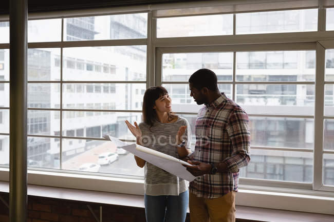 Front view of diverse business people discussing over blueprint in office at desk — Stock Photo