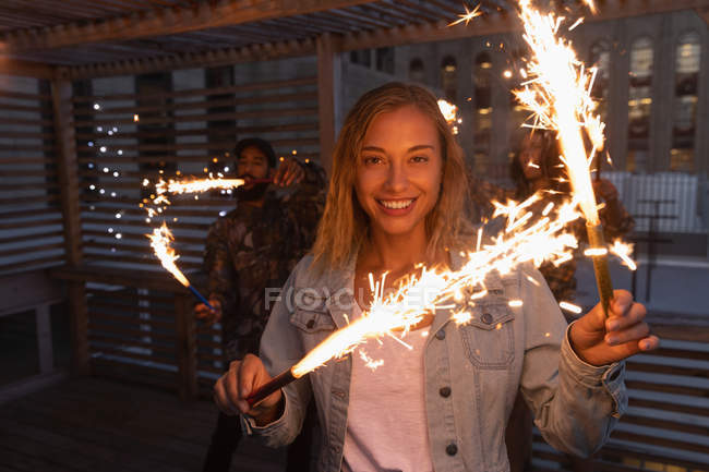Front view of woman enjoying sparkler in balcony while looking at camera — Stock Photo