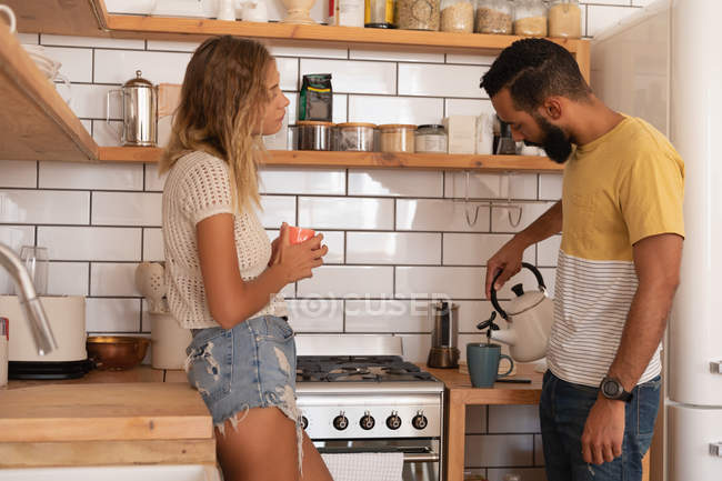 Вид сбоку на мультирасовую пару, беседующую друг с другом дома в кухонной комнате — стоковое фото