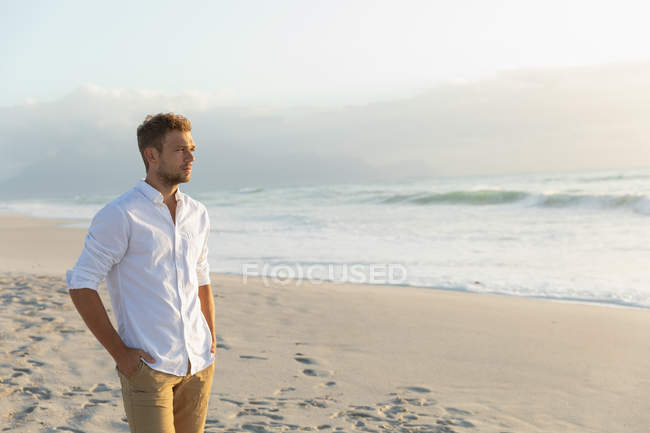 Vista lateral de homem bonito em pé na praia em um dia ensolarado. Ele está a ver a paisagem. — Fotografia de Stock