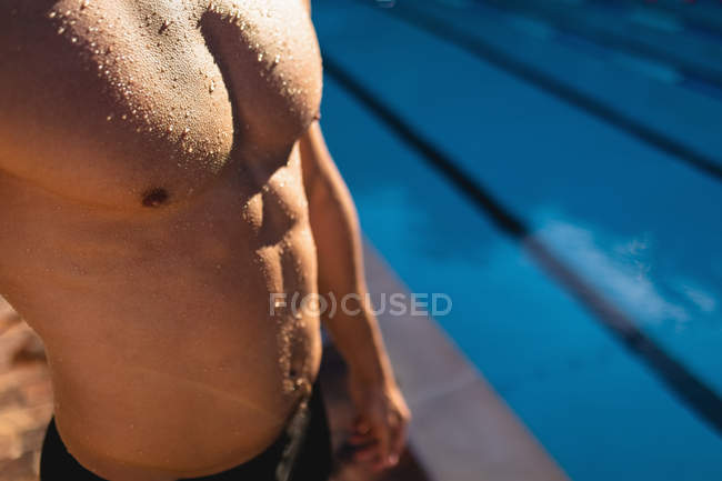 Sección media de un nadador masculino parado cerca de la piscina en un día soleado - foto de stock