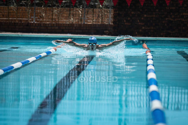 Вид спереди на молодого кавказского пловца с инсультом бабочки в открытом бассейне под солнцем — стоковое фото