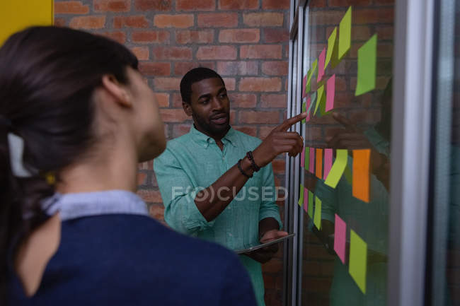 Vista lateral de diversos empresarios discutiendo sobre nota adhesiva en la oficina - foto de stock