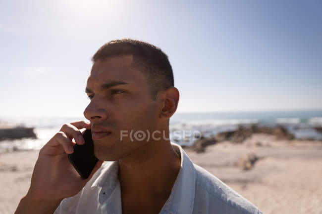 Nahaufnahme eines Mannes, der am Strand bei Sonnenschein mit dem Handy telefoniert — Stockfoto