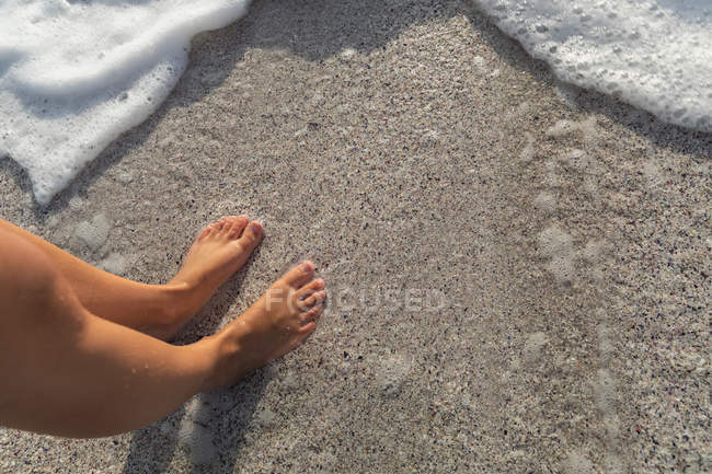 Low section of young woman tanned standing on sea foam at beach — Stock Photo