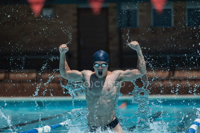 Front view of young Caucasian male swimmer with arms up celebrating victory in outdoor swimming pool in the sunshine — Stock Photo