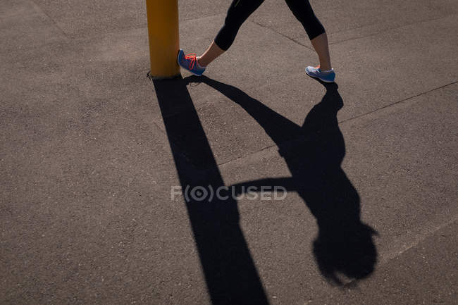 Unterteil einer aktiven Seniorin, die sich auf der Promenade in der Sonne gegen eine Stange reckt — Stockfoto