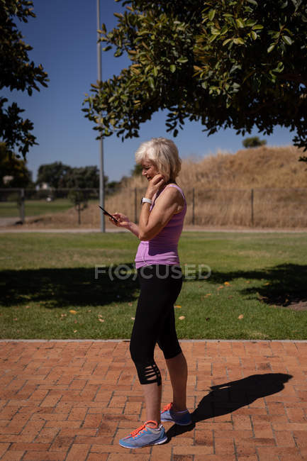 Vista lateral de uma mulher Sênior usando seu telefone celular no parque em um dia ensolarado — Fotografia de Stock