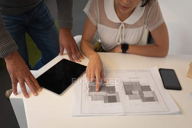 Mid section of multi ethnic business people discussing over a blueprint and touching it in the office — Stock Photo