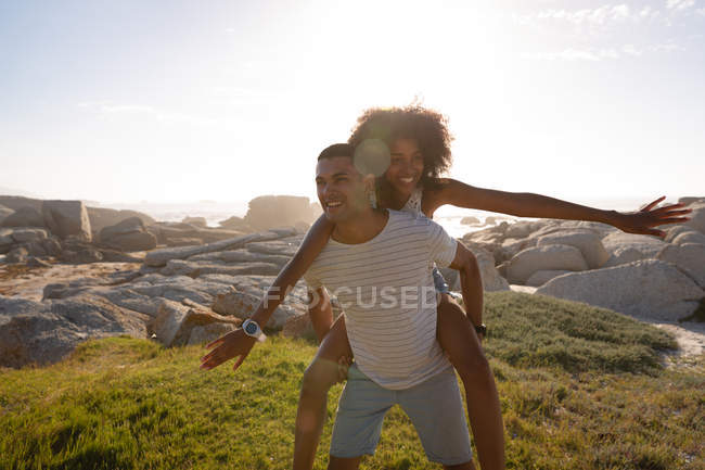 Vista frontal do homem afro-americano dando passeio de piggyback para a mulher perto do mar — Fotografia de Stock