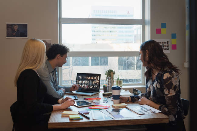 Вид сбоку деловых людей, обсуждающих фото на ноутбуке в офисе — стоковое фото