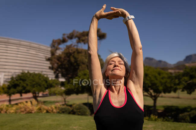 Вид спереду на активну старшу жінку, яка займається спортом і розтягується в парку в сонячний день — стокове фото