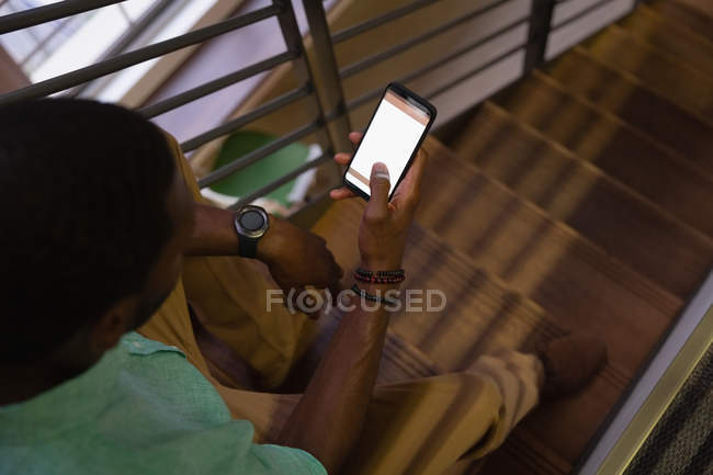 Vue en grand angle d'un homme d'affaires afro-américain utilisant un téléphone portable à l'escalier dans son bureau — Photo de stock