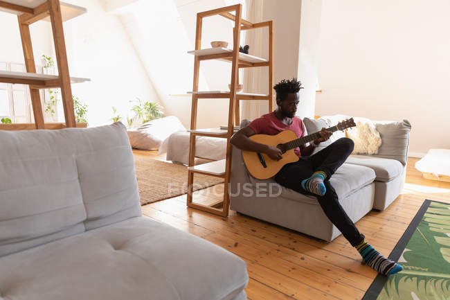 Vista laterale di African American Man seduto e suonare la chitarra in soggiorno a casa — Foto stock