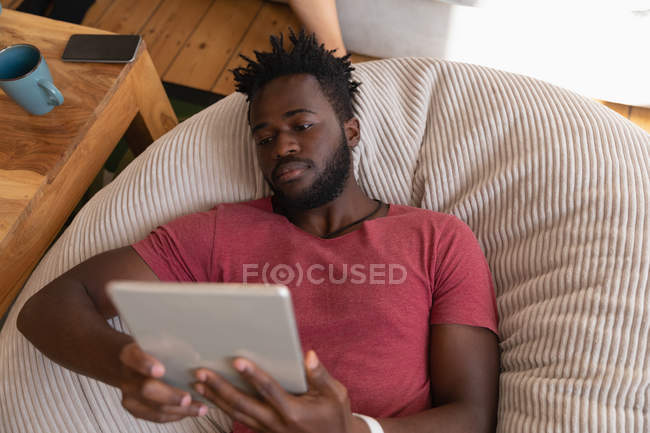 Visão de alto ângulo do homem afro-americano usando tablet digital na sala de estar em casa — Fotografia de Stock