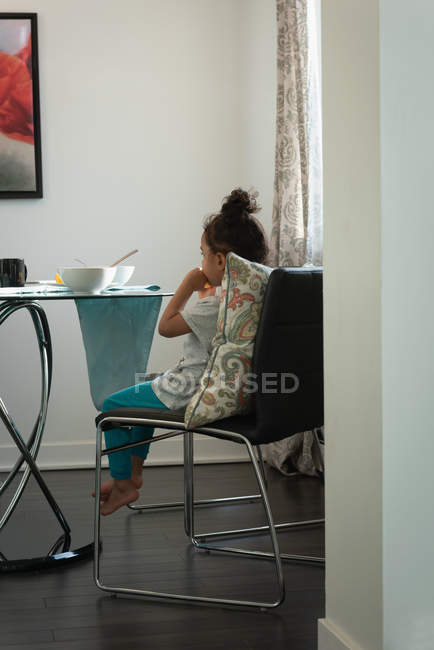 Vue arrière de la race mixte fille réfléchie assis triste à la maison tout en prenant le petit déjeuner à la maison — Photo de stock