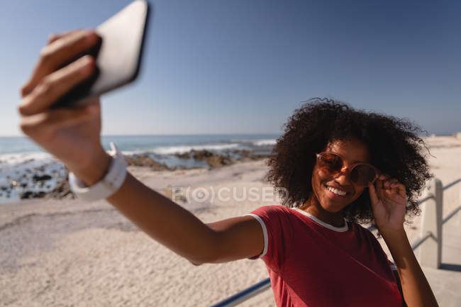 Front view of African-american woman taking selfie at beach on sunny day — Stock Photo