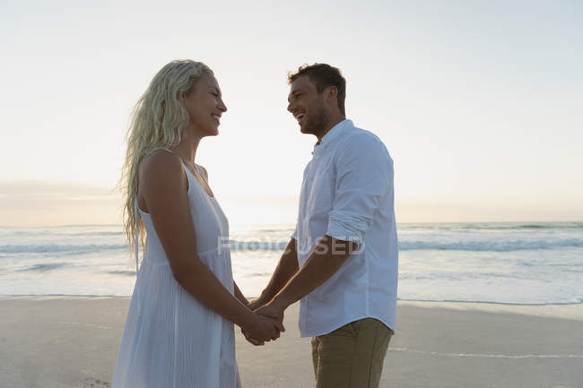Вид збоку молодої пари кохання тримає руки, стоячи на пляжі. Вони насолоджуються відпусткою — стокове фото