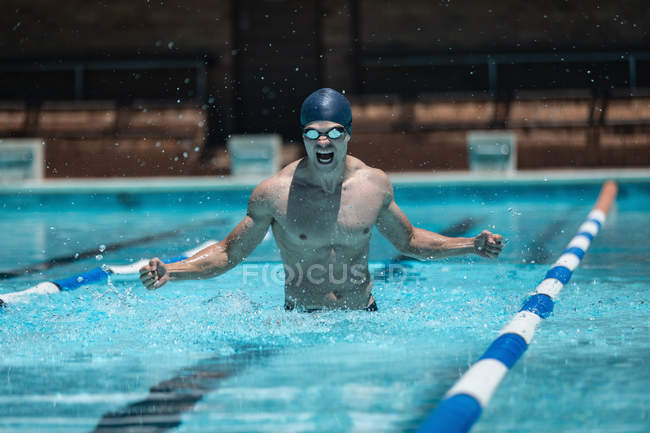 Front view of young Caucasian male swimmer with arms stretched out celebrating victory in outdoor pool in the sunshine — Stock Photo