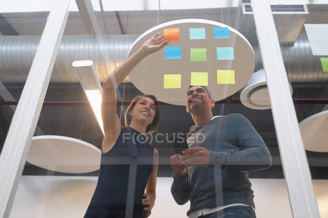 Low angle view of multi ethnic business people discussing over the sticky notes fixed on the wall in office — Stock Photo