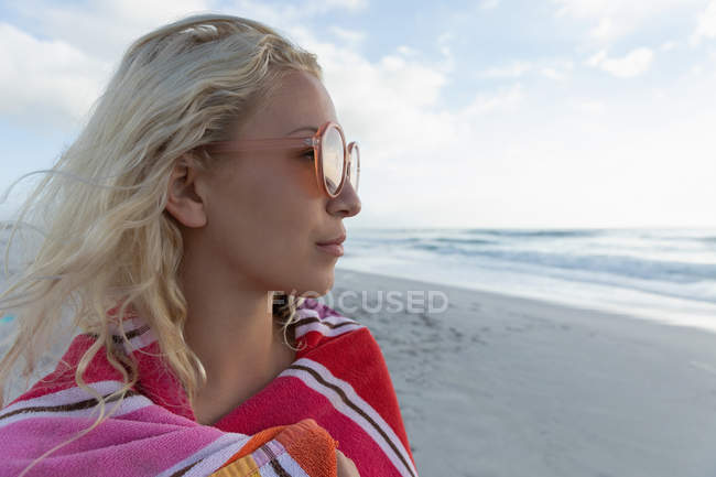 Seitenansicht einer blonden Frau, die an einem sonnigen Tag am Strand steht. sie trägt eine Sonnenbrille und beobachtet den Ozean — Stockfoto