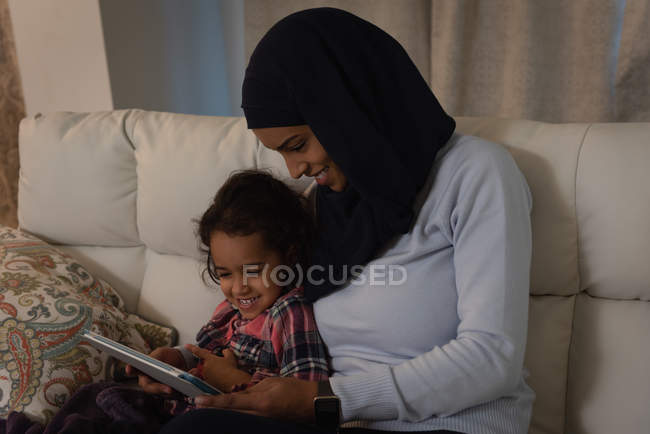 Вид спереду Мати в хіджабі і дочка в хіджабі, використовуючи цифровий планшет вдома на дивані — стокове фото