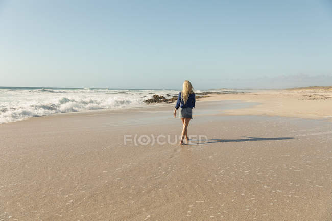 Rückansicht einer entspannten blonden Frau, die an einem sonnigen Tag am Strand spaziert — Stockfoto