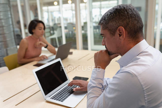 Seitenansicht eines nachdenklichen Geschäftsmannes, der an seinem Laptop arbeitet und im Büro am Schreibtisch sitzt — Stockfoto