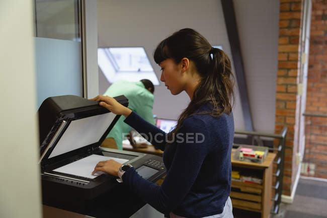 Вид сбоку на вдумчивую деловую женщину, использующую ксерокс в офисе — стоковое фото