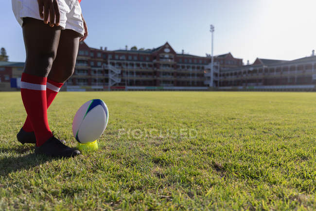 Seção baixa de um jogador de rugby masculino se preparando para chutar a bola no chão de rugby em um dia ensolarado — Fotografia de Stock