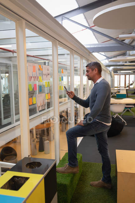 Vista lateral del hombre de negocios capturando fotos de notas de palo fijadas en la pared en la oficina - foto de stock