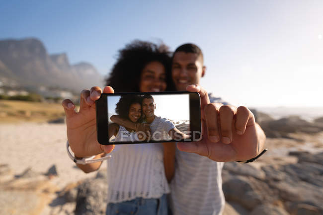 Vorderansicht des Paares, das lächelnd am Meer steht und ein Selfie macht — Stockfoto