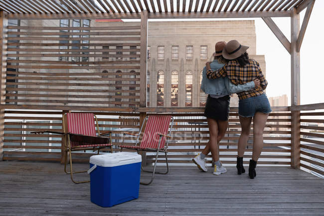 Visão traseira de várias amigas étnicas de pé de volta para a câmera com o braço ao redor na varanda em casa — Fotografia de Stock