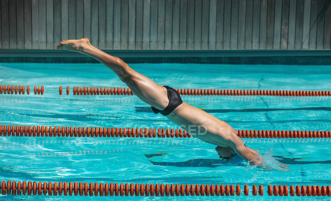 Vista laterale del giovane nuotatore maschio caucasico che si tuffa nell'acqua di una piscina nella giornata di sole — Foto stock