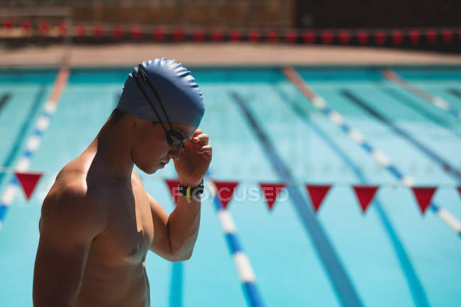 Vista lateral de un joven nadador caucásico de pie en la piscina bajo el sol - foto de stock