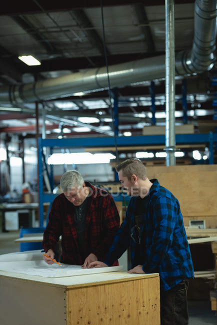 Frontansicht männlicher Tischler beim Diskutieren und Messen in der Werkstatt — Stockfoto