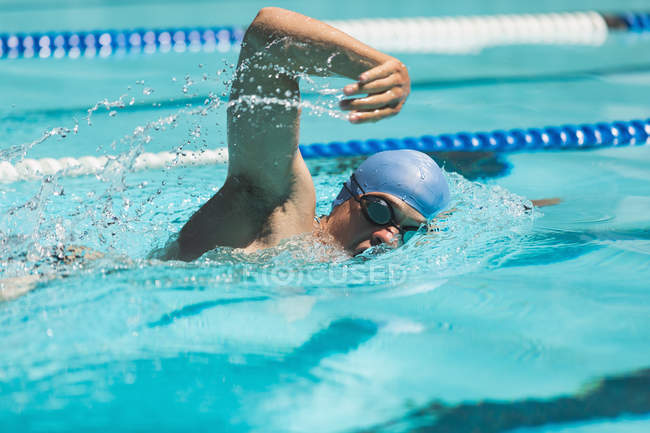 Gros plan du jeune nageur masculin caucasien nageant libre dans la piscine extérieure au soleil — Photo de stock