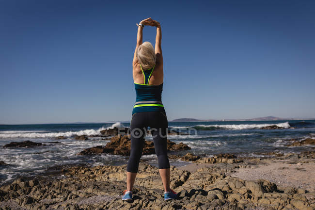 Rückansicht einer aktiven Seniorin, die am Strand unter der Sonne trainiert — Stockfoto