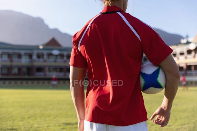 Вид сзади на игрока в регби, держащего мяч для регби и стоящего на стадионе — стоковое фото