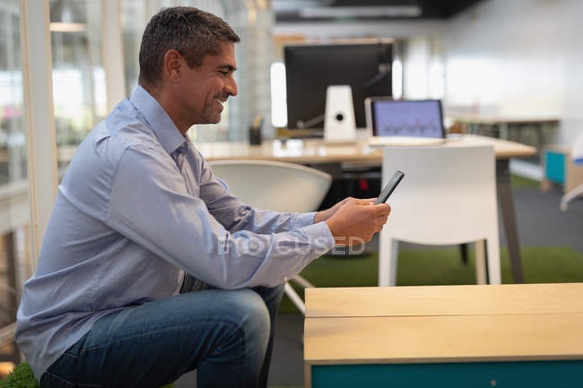 Вид сбоку бизнесмена с мобильного телефона, сидящего на синтетической травяной скамейке в офисе — стоковое фото