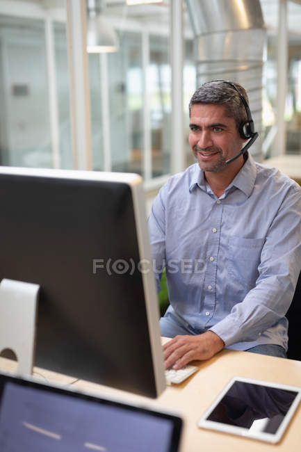 Frontansicht eines Geschäftsmannes, der mit seinem Computer und einem Headset am Schreibtisch im Büro arbeitet — Stockfoto