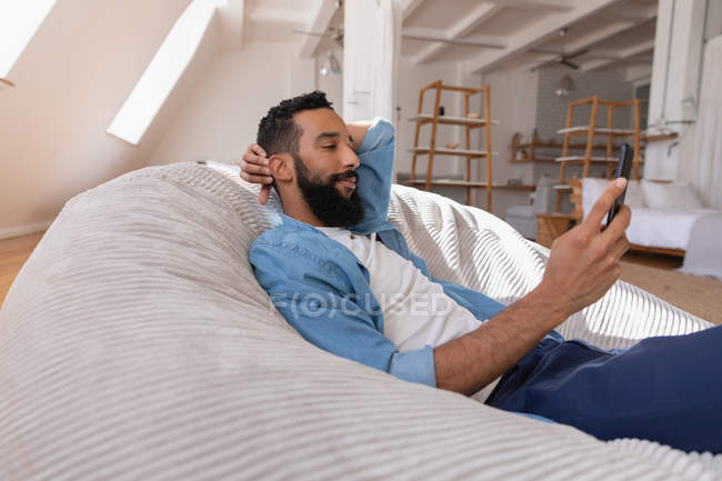 Seitenansicht eines Mannes, der sein Handy zu Hause benutzt, während er sich lehnt — Stockfoto