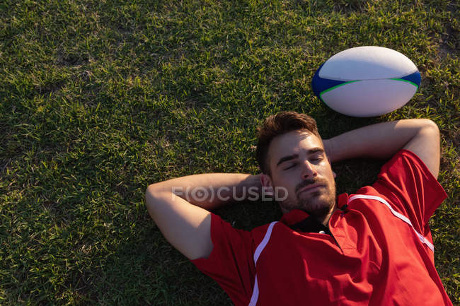 Високий кут зору розлюченого чоловіка регбіста, що лежить з м'ячем регбі на стадіоні — стокове фото