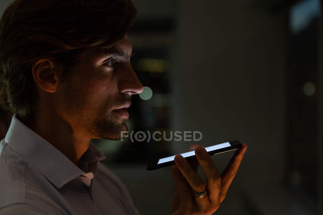 Vista lateral de belo jovem executivo do sexo masculino falando no telefone celular em um escritório moderno — Fotografia de Stock