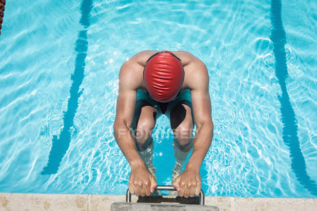 High angle view of young Caucasian male swimmer holding starting block in outdoor swimming pool on sunny day — Stock Photo