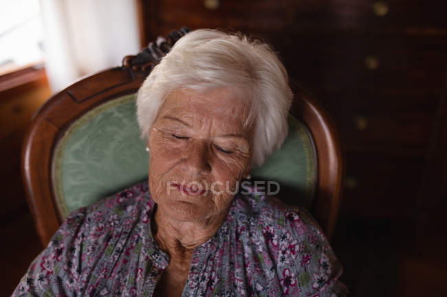 Vista frontal de una mujer mayor durmiendo en un sillón en la sala de estar en casa - foto de stock