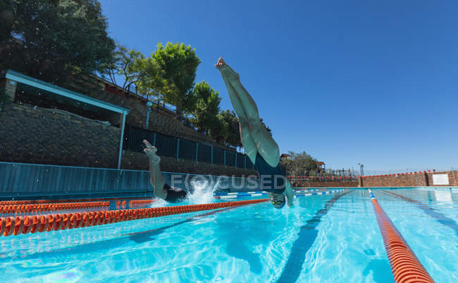 Visão de baixo ângulo de nadadores caucasianos masculinos e femininos pulando na água ao mesmo tempo na piscina ao sol — Fotografia de Stock