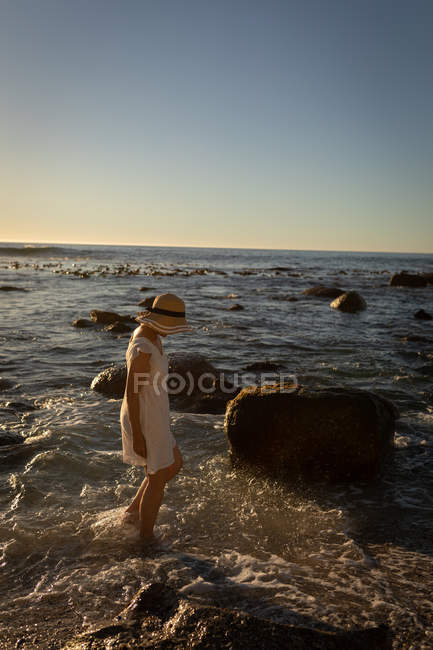 Seitenansicht einer aktiven Seniorin, die am Abend am Strand auf dem Wasser spaziert — Stockfoto